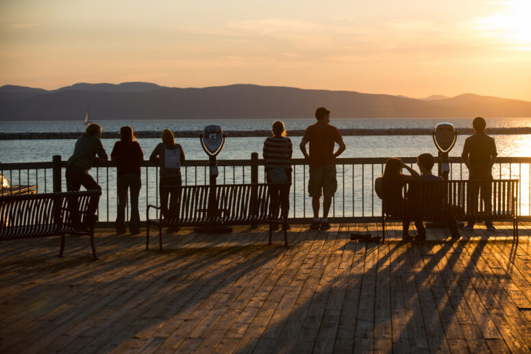 Image of people standing on the Burlington Waterfront boardwalk looking at the sunset